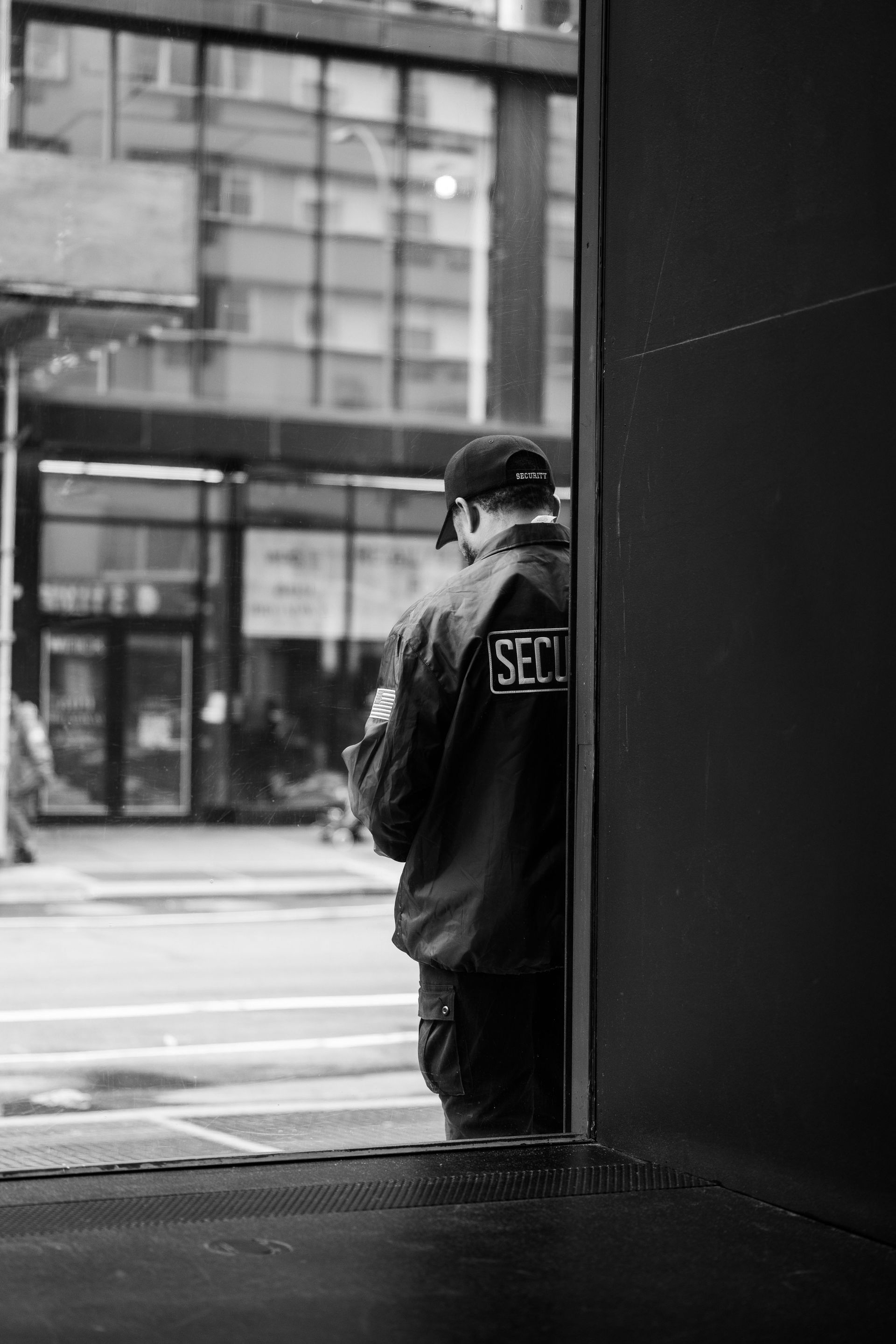A solitary security guard stands in an urban street, captured in monochrome, evoking a sense of loneliness.
